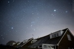 Stars fill the night sky above suburban rooftops
